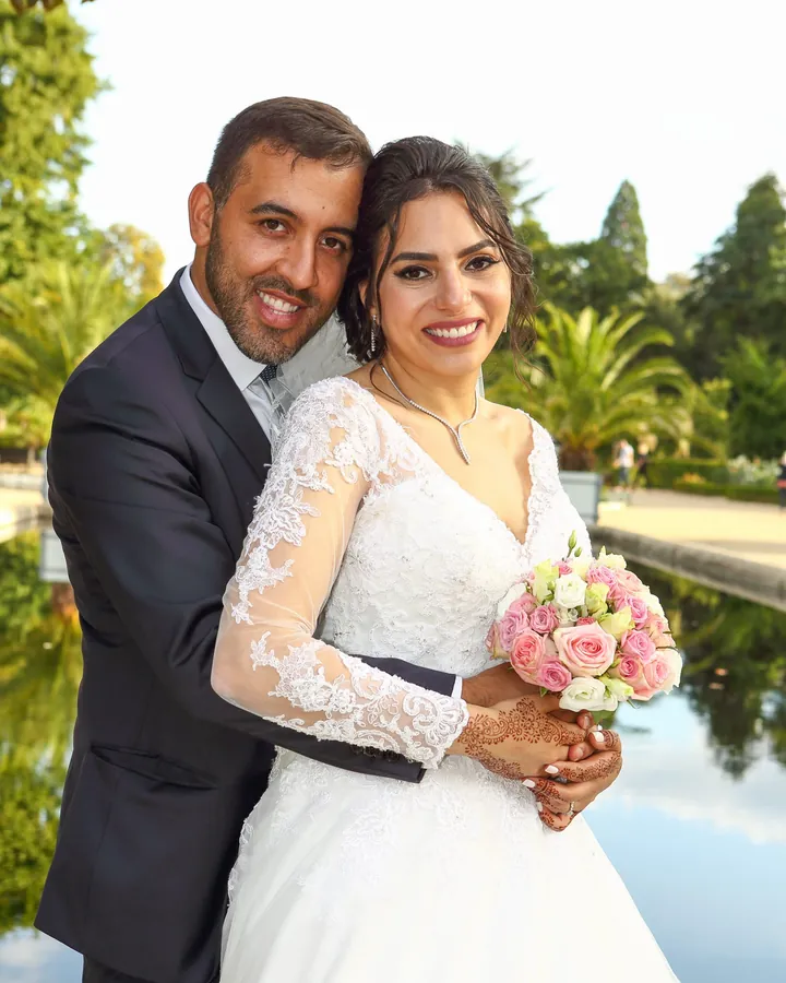 Mariés enlacés au bord d'un bassin, bouquet de roses à la main